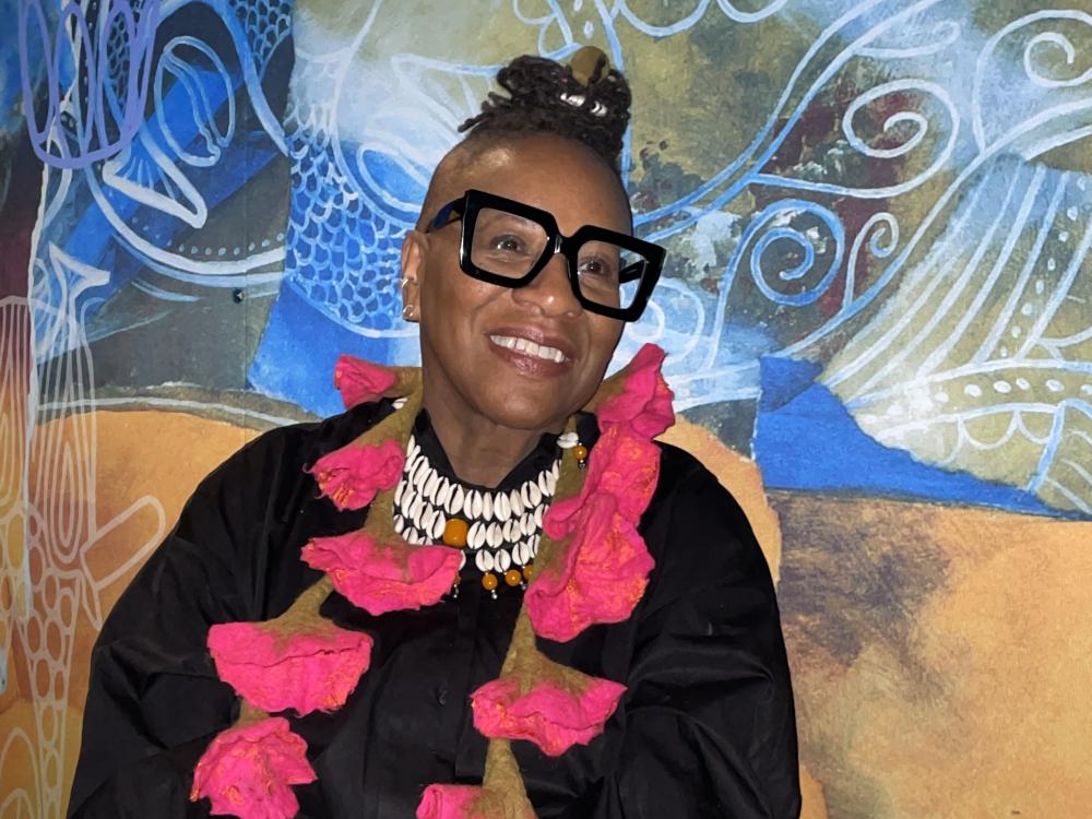 Black woman with hair on top of her head, black glasses and bright pink necklace