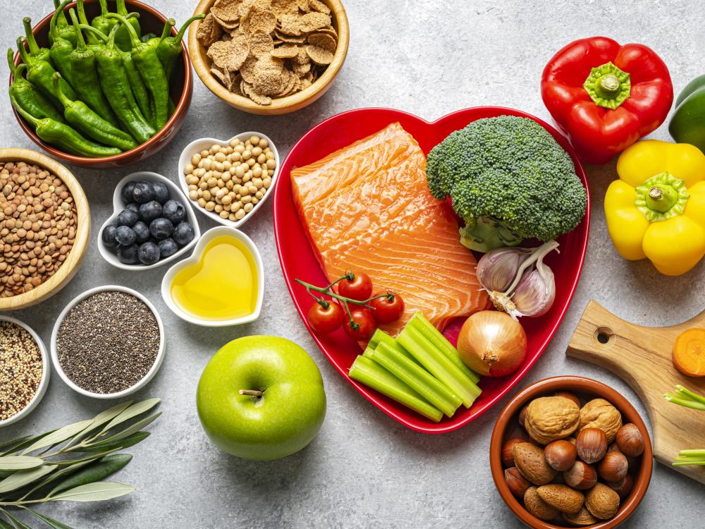 healthy foods in bowls and on a clean counter, including raw salmon steak, vegetables, olive oil, and nuts