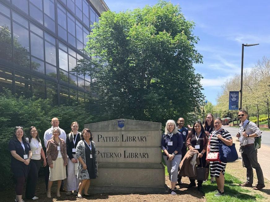 A group poses for a photo with the Patee and Paterno Libraries sign