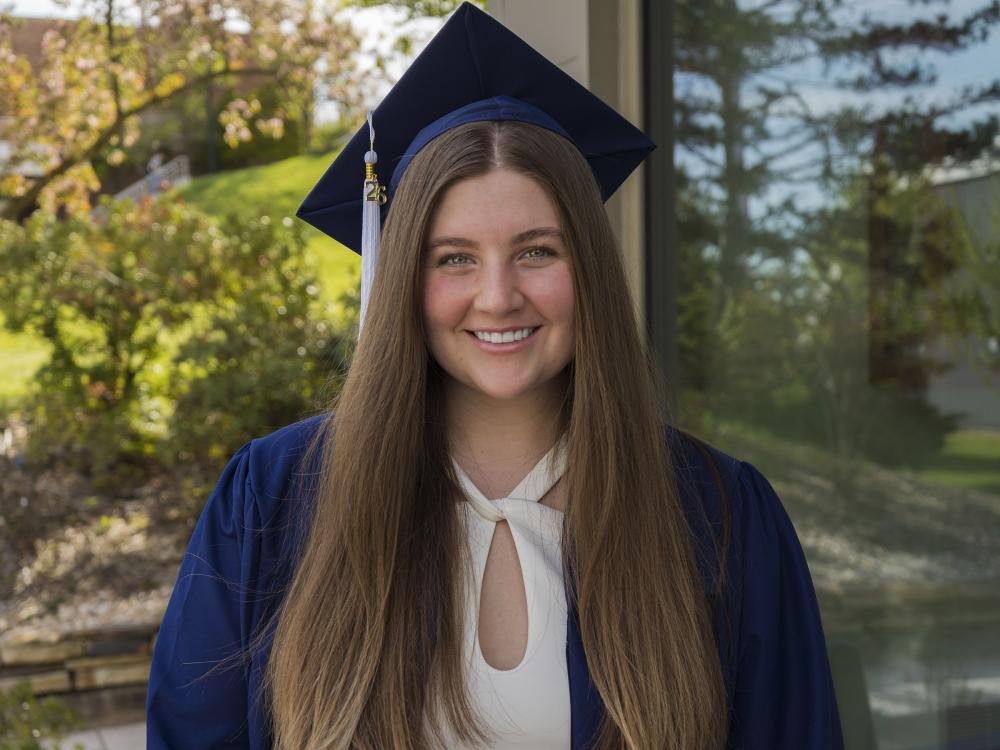 Penn State female graduate smiles for a photo wearing blue commencement reglia. 