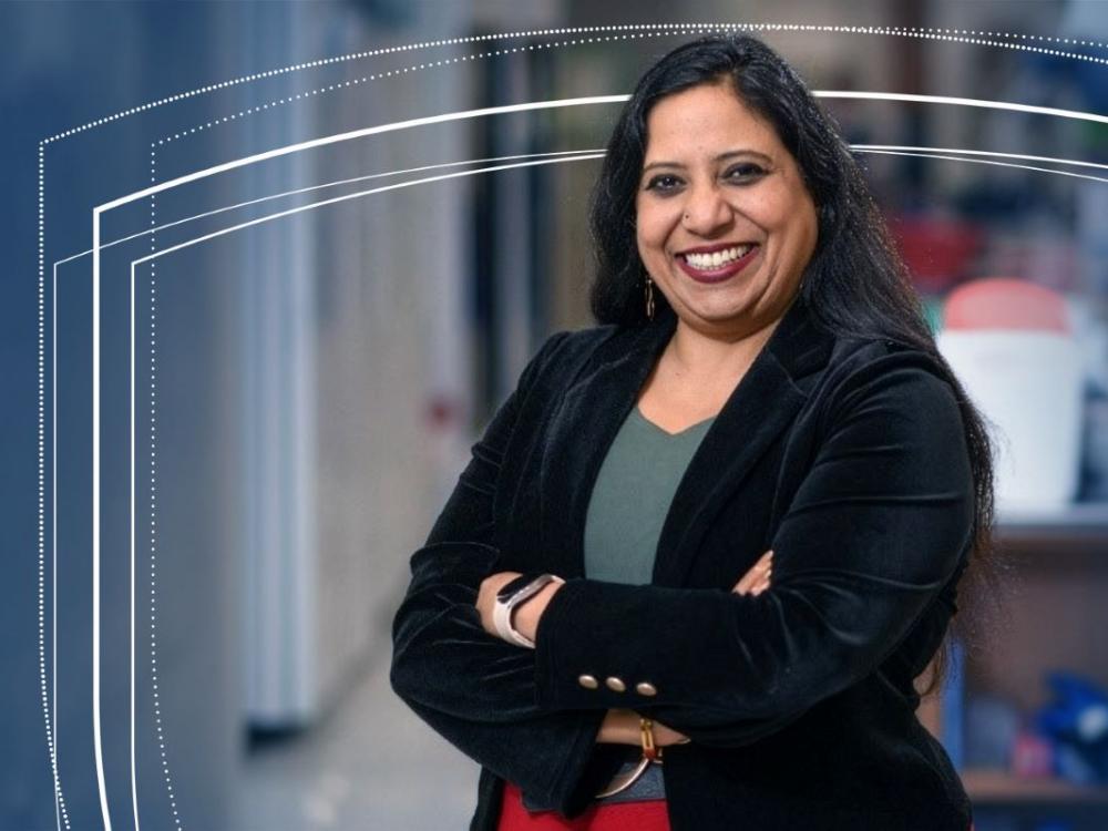 Indira Mysorekar poses for a professional portrait with arms crossed in an indoor setting.