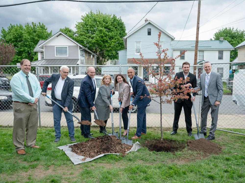 A group of people plant trees. Most have shovels in hand.