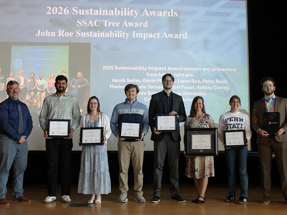 The 2025-26 Roe Award winners at the recognition ceremony stand on a stage with their awards against a projected slideshow background.