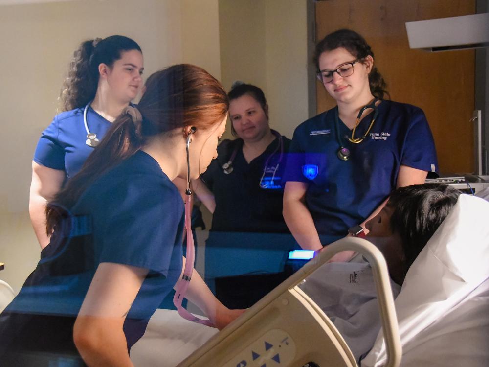 Four nursing students in blue uniforms attend a training manikin