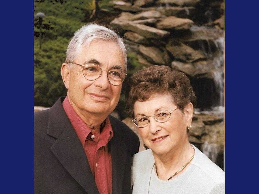 A photo portrait of an elderly white man with grey hair and glasses and an elderly white woman with dark hair and glasses