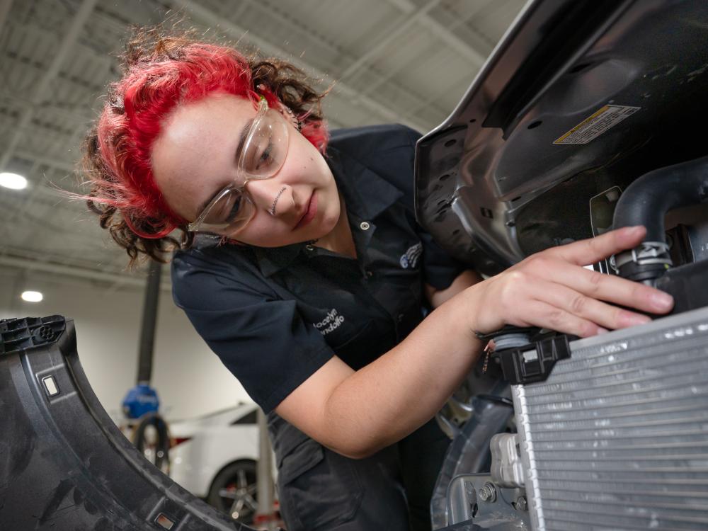 A red-haired young woman student works on a car