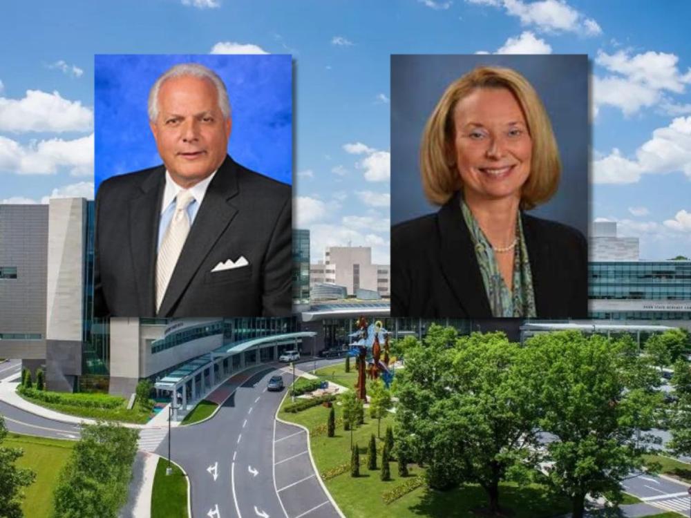 Composite image showing two professional headshots positioned above the entrance of a large modern hospital building. The headshot on the left features a man in a dark suit and light tie against a blue background. The headshot on the right features a woman in a dark blazer and patterned scarf against a gray-blue background. The hospital campus is visible below, with glass-fronted architecture, a circular drive, trees, and a partly cloudy sky.