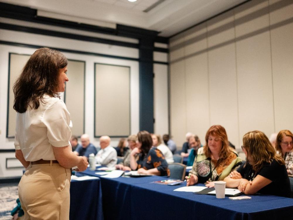 Presenter leading workshop session while attendees listen, take notes, and participate in discussion at a business conference.
