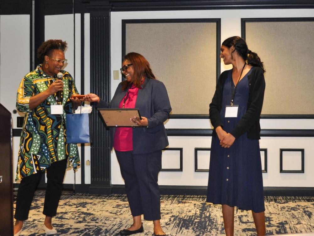 Lori Francis presents Melody Goodman with a gift while standing next to Sanjana Murthy.