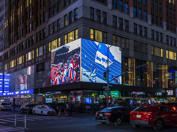 Image of a busy city street at night with two large video boards displaying animated art work
