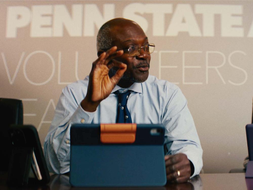 Ron Darbeau sitting at a table with a tablet device in front of him and the words Penn State Volunteers on the wall behind him.