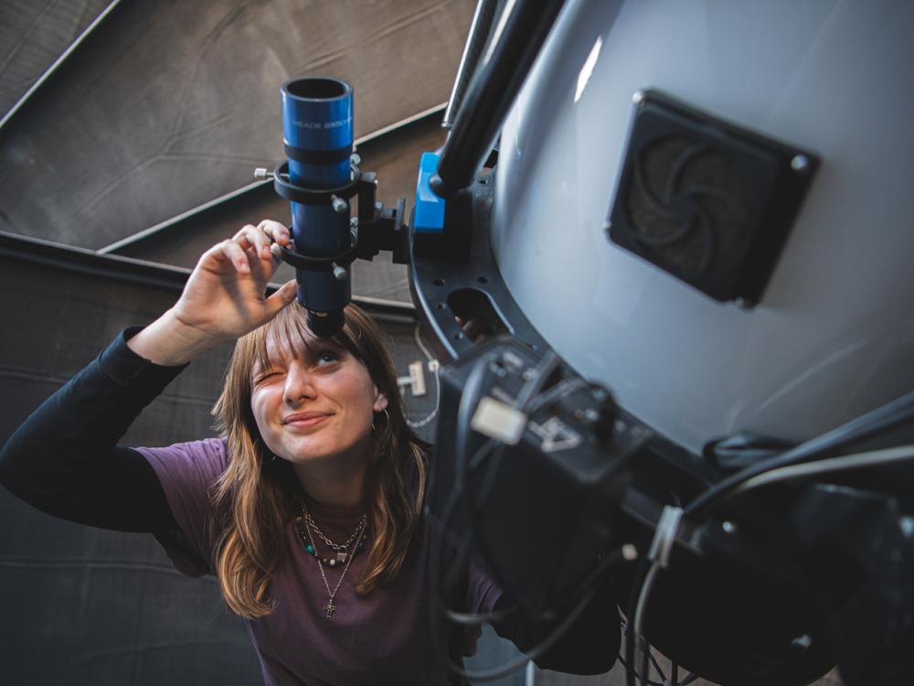 woman in purple shirt looks through telescope 