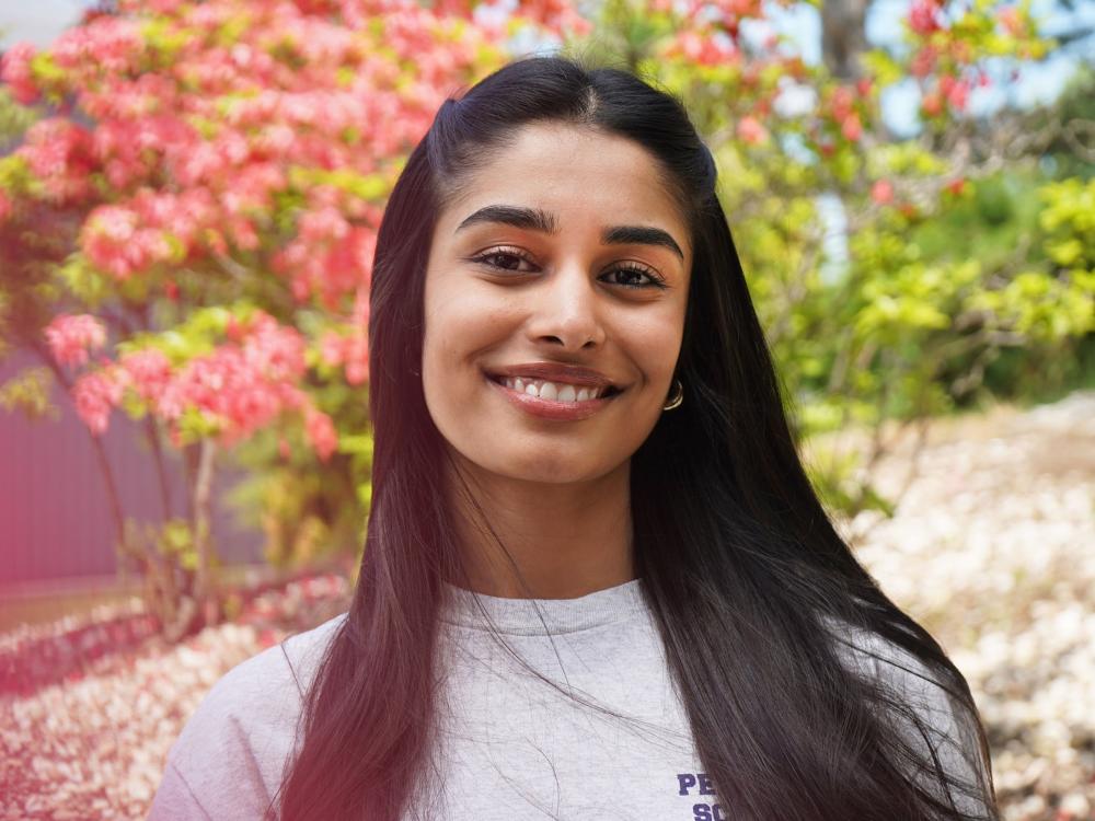 Female student wearing Penn State Scranton shirt smiles with red floral trees in background.