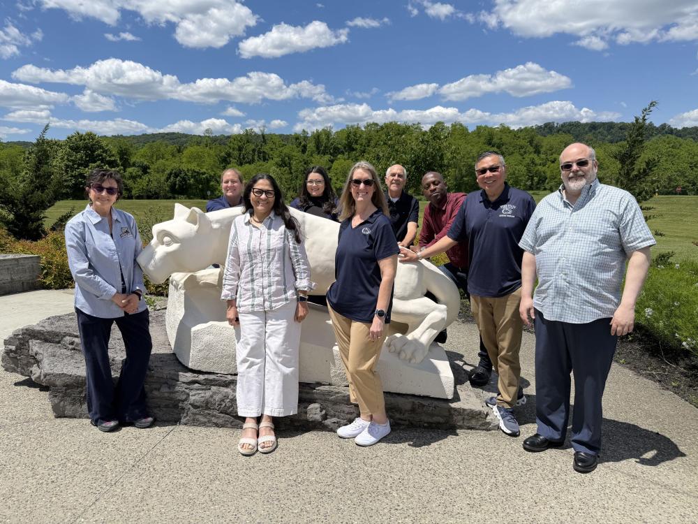 group of people standing together for a photo in front of the nittany lion statue