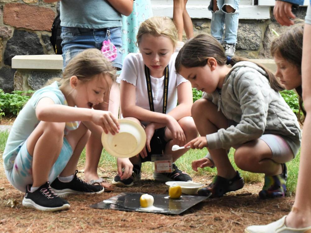 Three young girls crouch over food on aluminum foil during a youth science project.