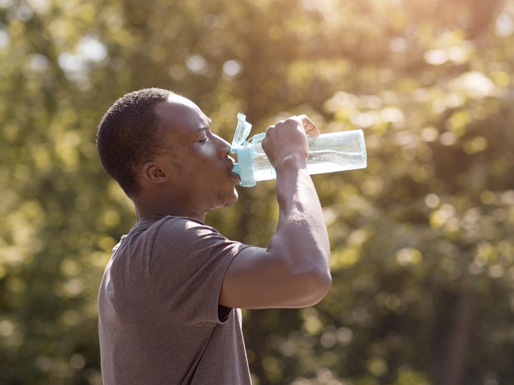 A thirsty man in the sun drinks a bottle of water.