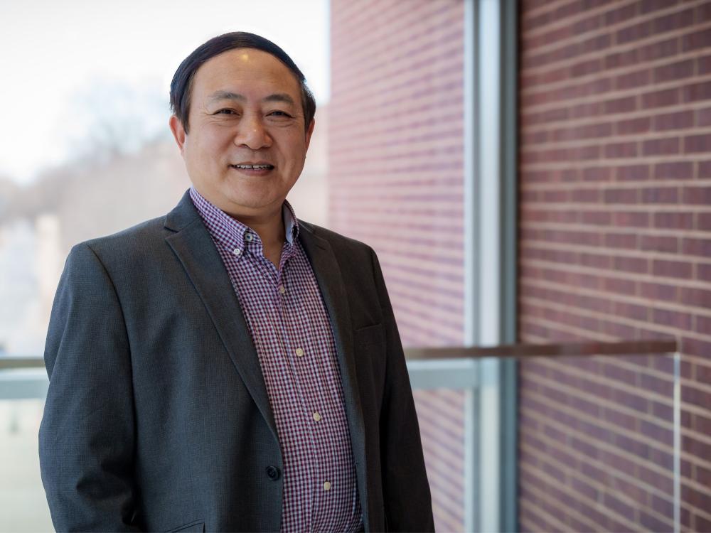 college professor with dark hair and suit jacket in glass and brick campus building