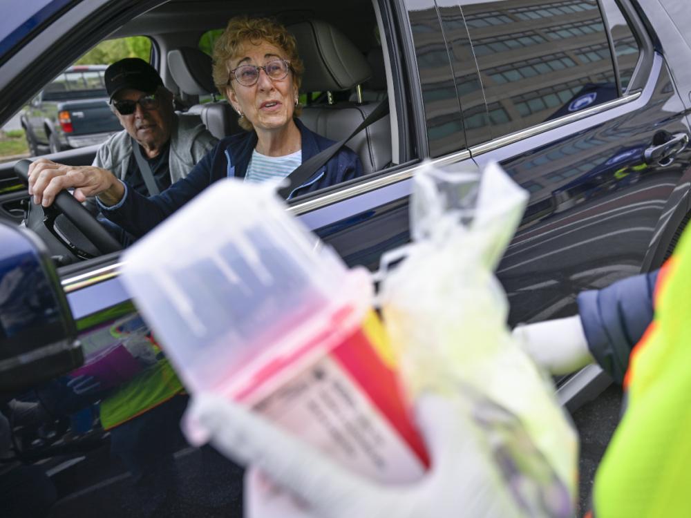 A man and woman sitting in a car talk to a person at Penn State Health’s Prescription Drug Take-Back Day. The person holds a sharps container and is wearing a safety jacket and coat.
