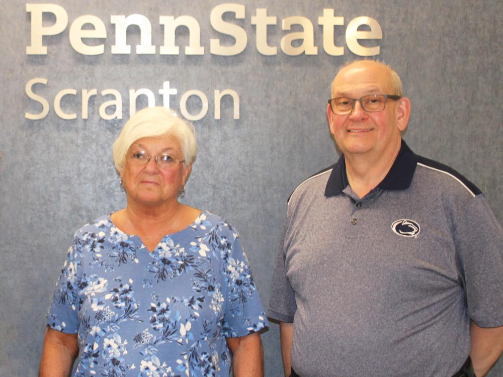 Joette Dempsey and Ed Lucy pose for a photo in front of wall with Penn State Scranton name