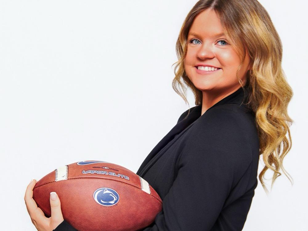 Smiling girl with shoulder length brown holding football in her left arm.