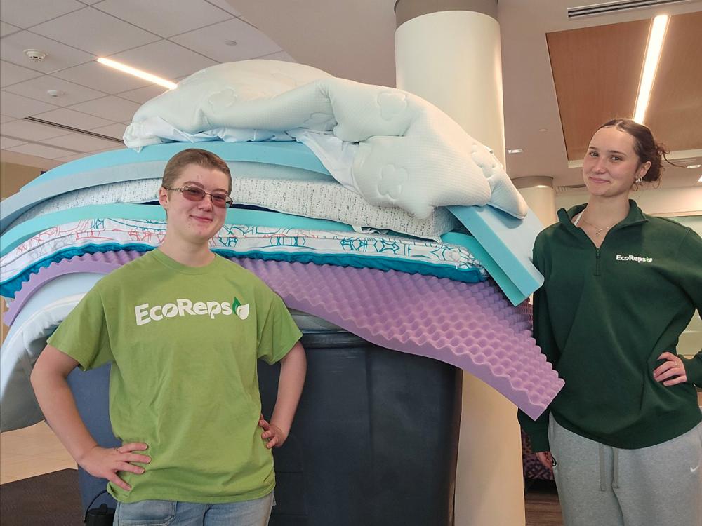 Two students stand in front of a stack of mattress toppers collected during the move-out period in May.