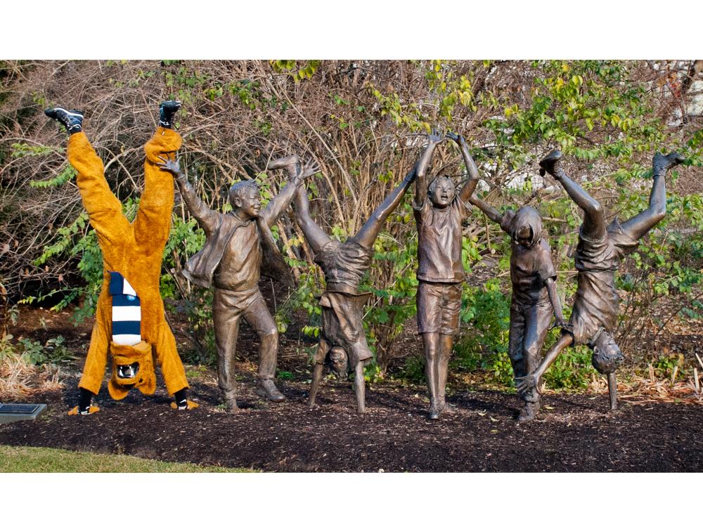 The Nittany Lion mascot does a handstand next to a sculpture outside