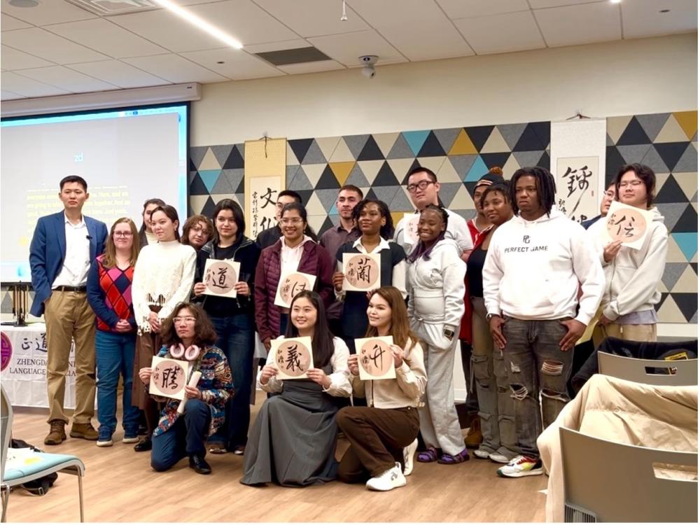 A group of students stand with calligraphy art pieces in a lecture hall.