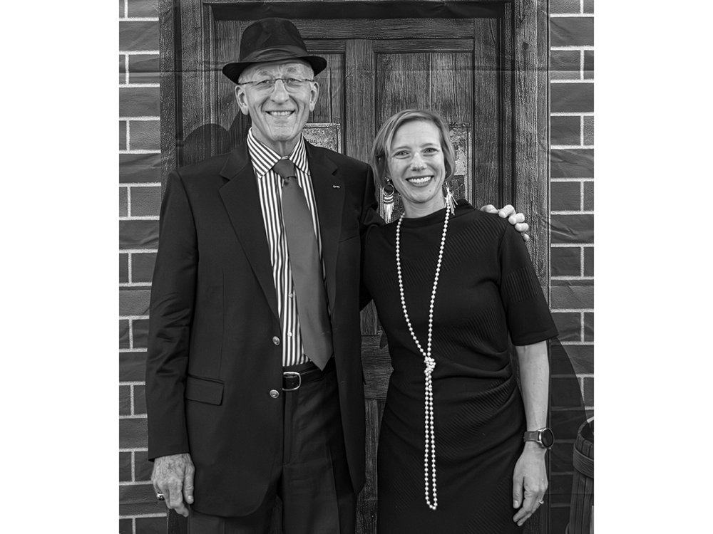 Two people pose for a black and white photo wearing speakeasy-era clothes.