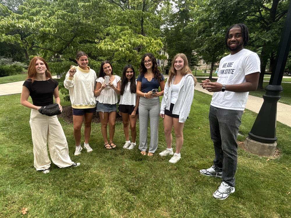 Six students standing on a grassy campus area