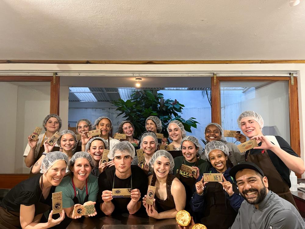 Professors Alicia Drais-Parrillo and Cathleen Hunt, bottom left, pose with students and a workshop instructor, bottom right, during a chocolate-making workshop, displaying their handmade chocolate.
