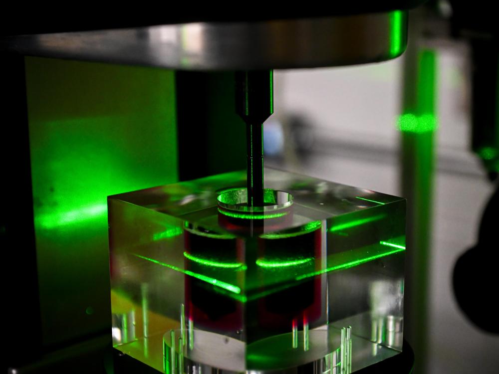 Device with green laser light shining on red liquid in beaker