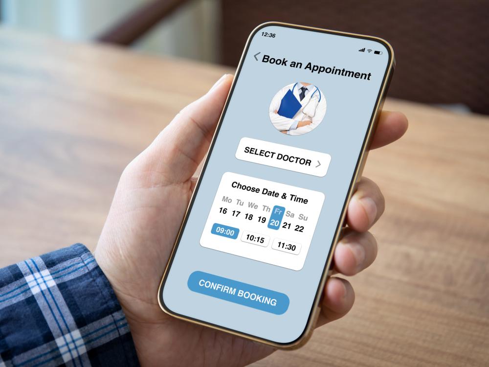 A hand holding a smartphone with a telehealth app on the screen. The app is confirming an appointment booking for Friday, the 20th at 9:00 a.m.