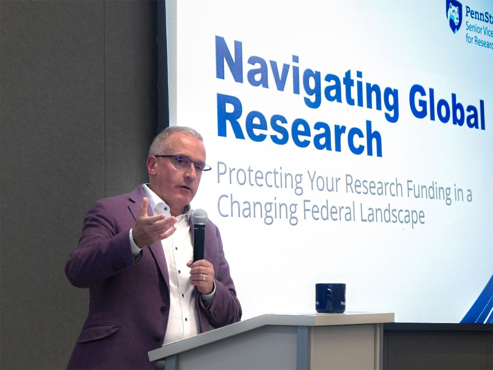 Andrew Read, senior vice president for research, speaking at a podium in front of a slide that reads "navigating global research"