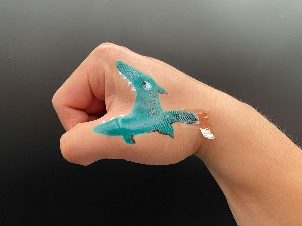 A close up shot of a bioelectrode painted to look like a shark on the side of a researcher's curled fist