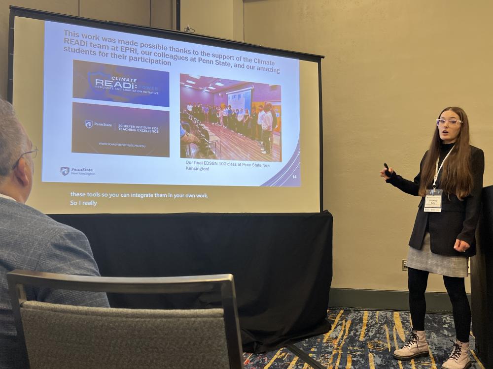 A conference presenter stands beside a projection screen displaying a slide about climate resilience, adaptation and engineering education during a conference session. Audience members are seated facing the screen, and the slide includes references to Penn State, the Schreyer Institute for Teaching Excellence and the Climate READi initiative.