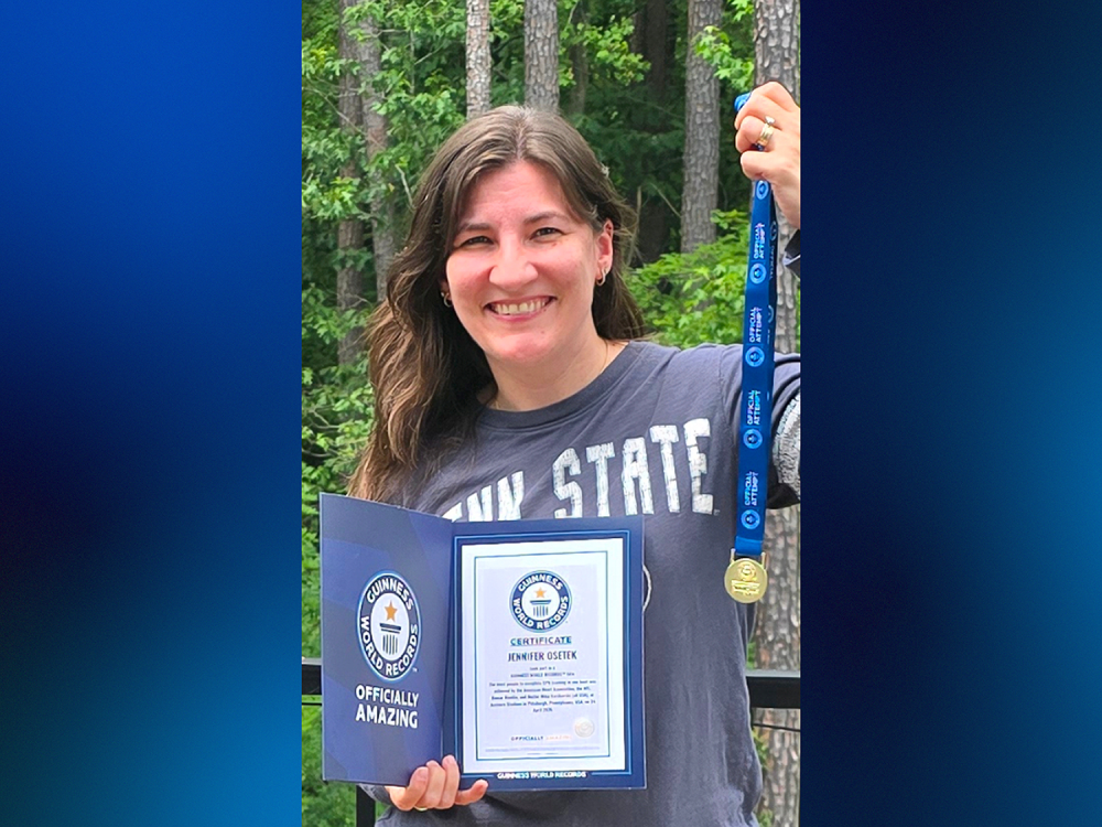 A woman holds a meal and certificate in front of trees.