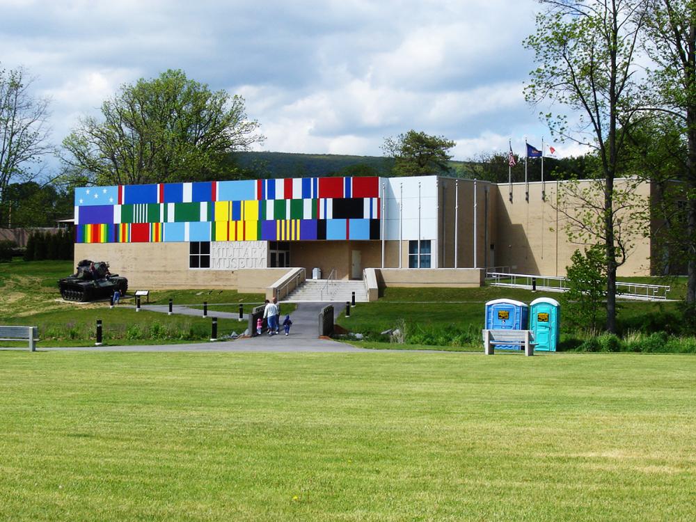 Pennsylvania Military Museum in Boalsburg with a colorful flag mural across the front under a cloudy sky.