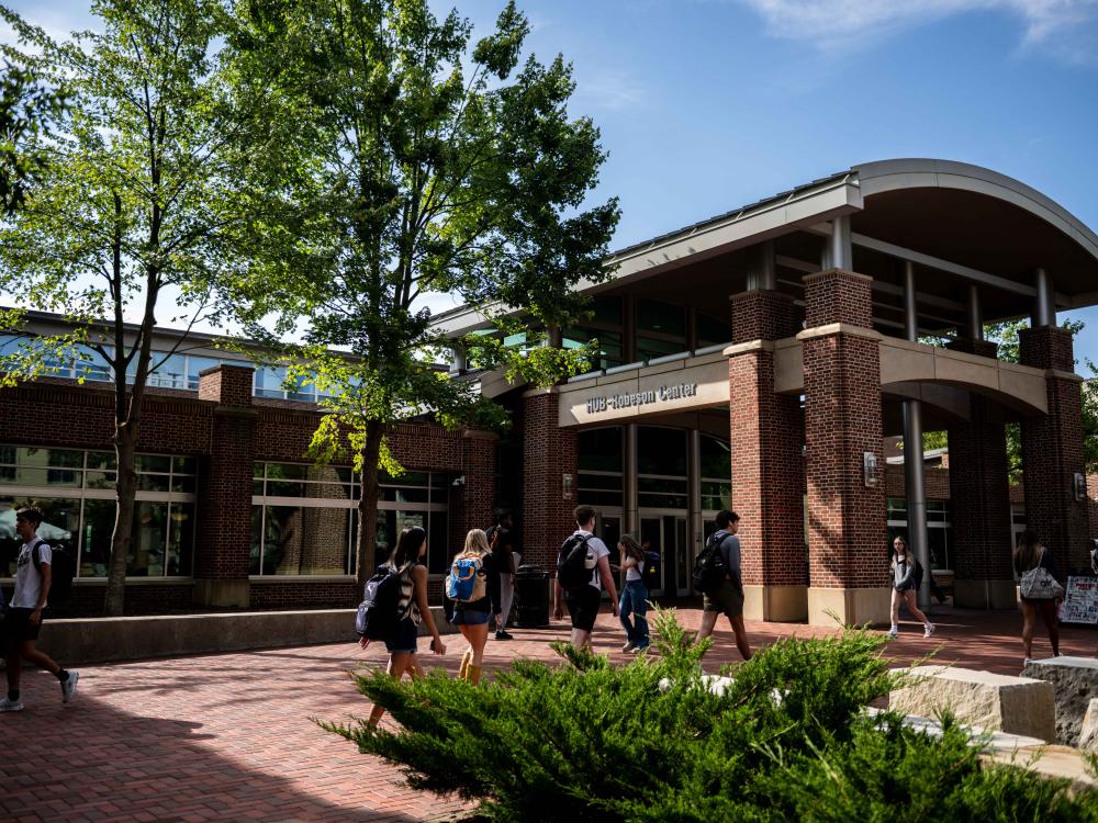 Students carrying backpacks walk along a brick plaza outside the HUB-Robeson Center on a sunny first day of fall classes