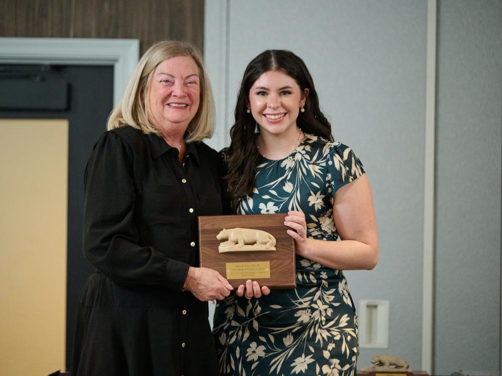 Laurie Badzek stands to the left of Kaléi Crimi, who holds an award plaque.