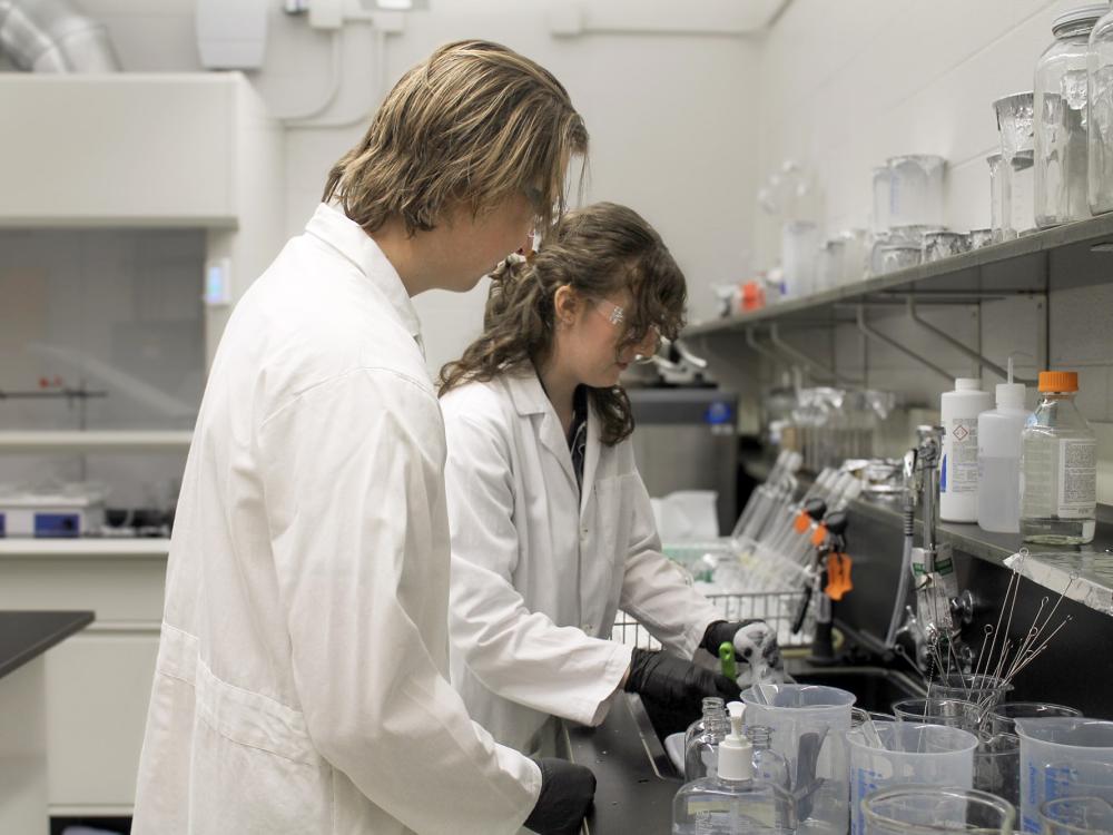 Two students in white lab coats wash equipment in a lab as part of Penn State's Sustainable Labs Program
