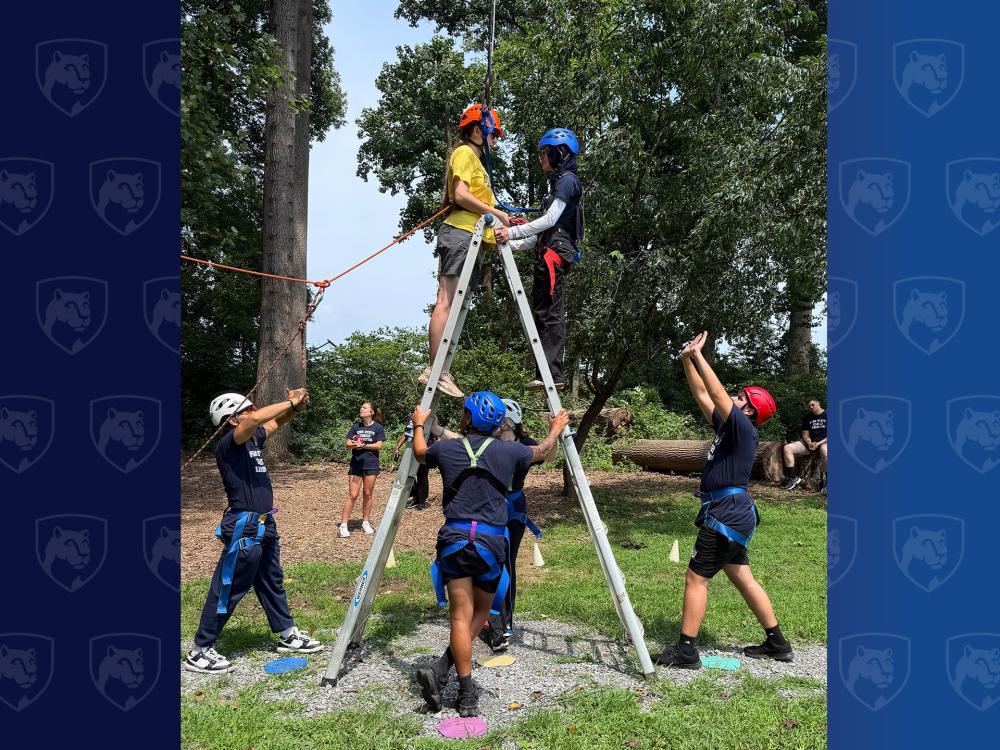 students on a ladder with others helping them