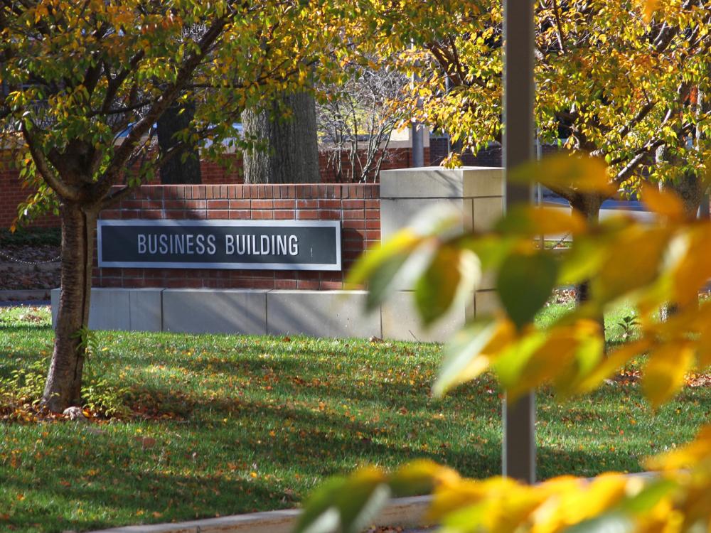 A sign reading Business Building on the Penn State University Park Campus surrounded by leaves and grass