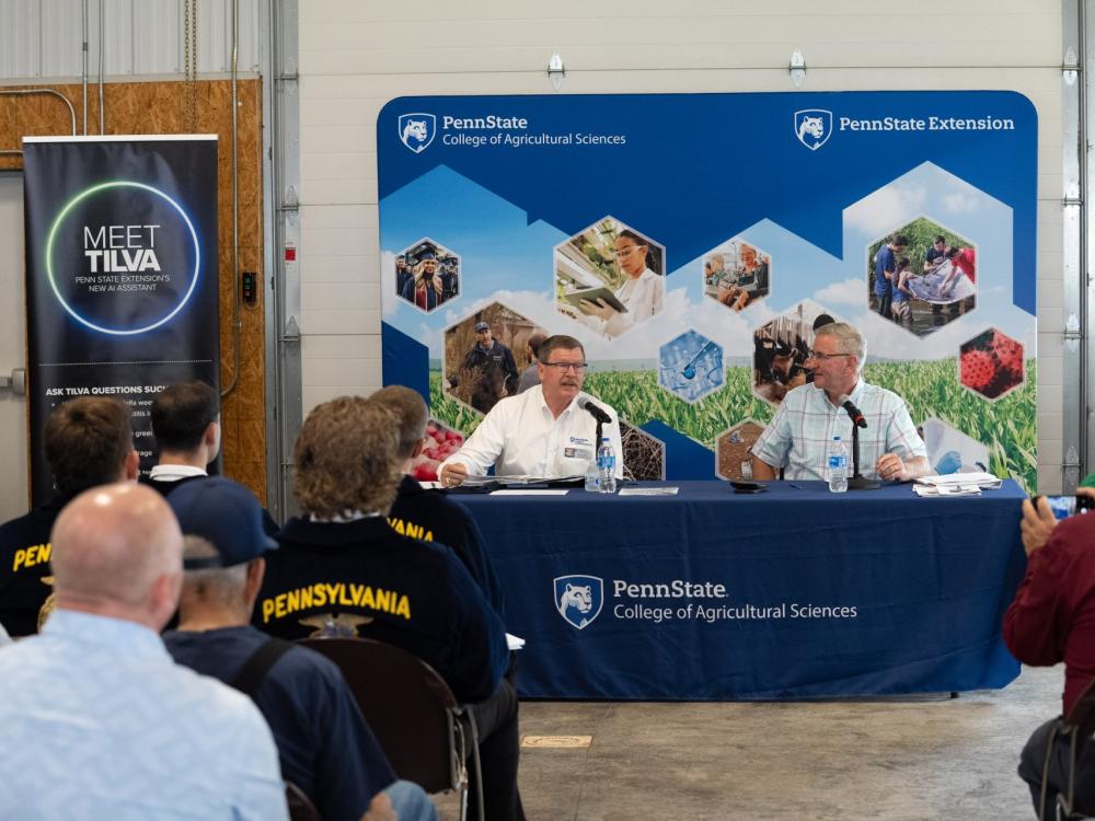 Two men speak on a panel at a Penn State agricultural town hall as an audience listens.