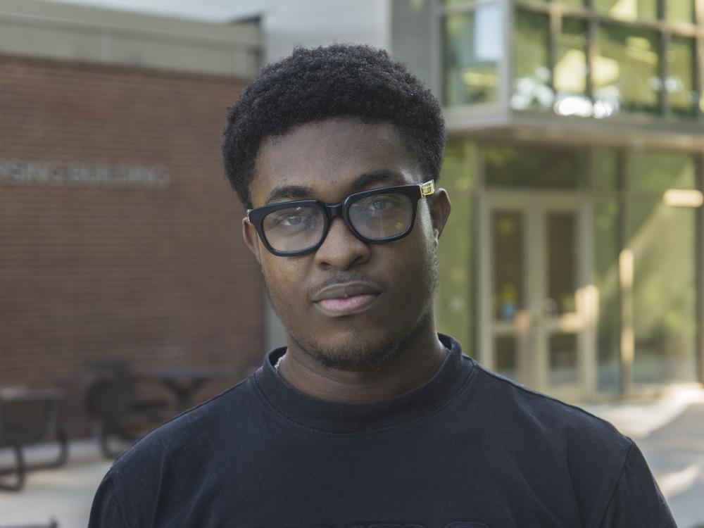Male student wearing glasses stands in front of brick building