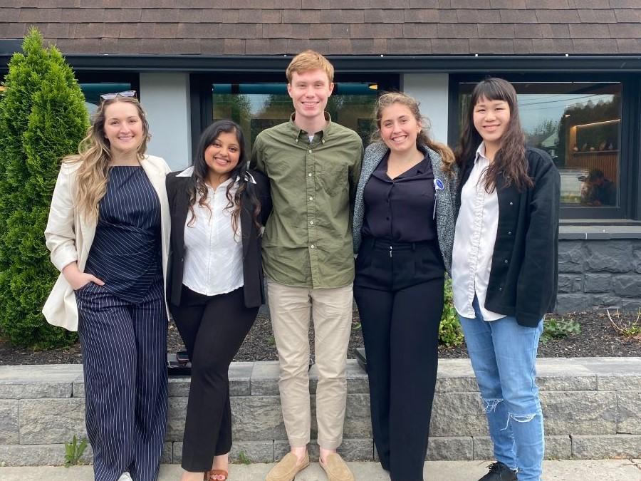 A group of five students stands outside of a building for a group photo.