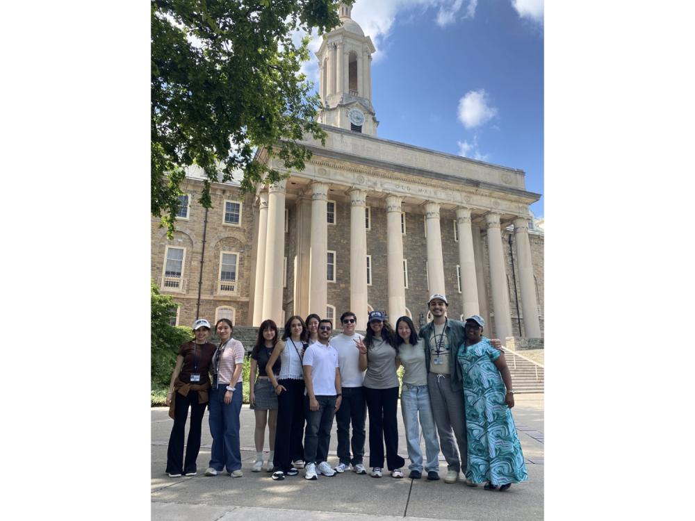 Students stand for a group photo in front of a large building on the University Park campus.