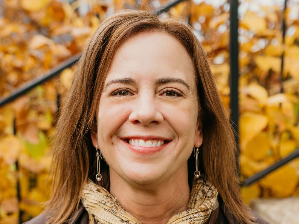 Heather Stephens, a woman with medium-brown hair smiling. Gold leaves in the background