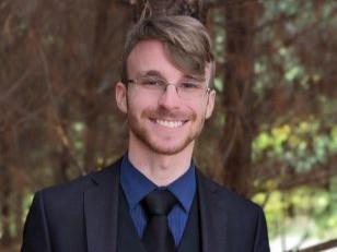 Young man in a suit and tie and glasses posing outside