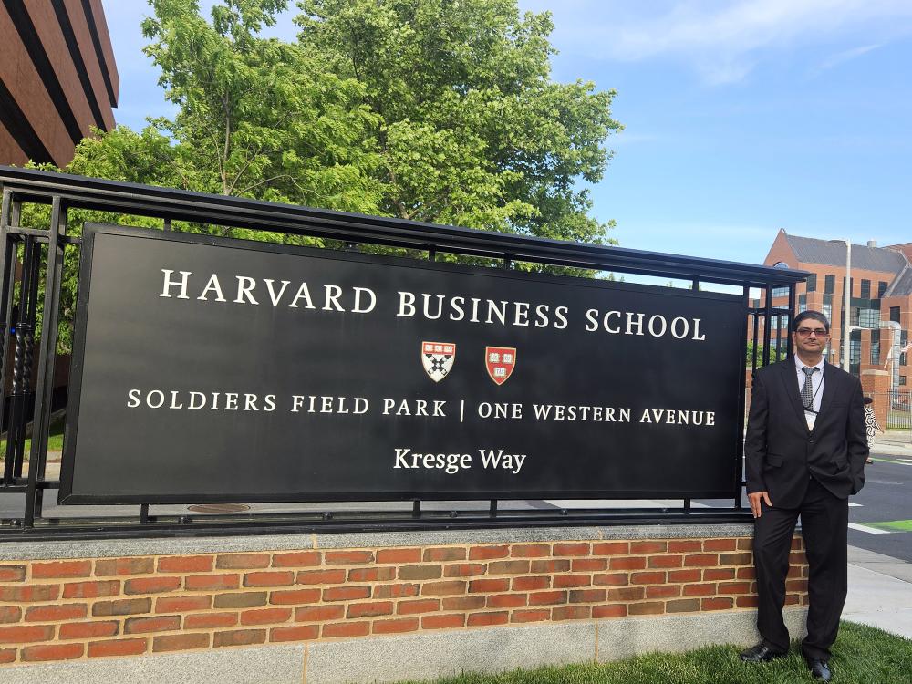 Man in a suit stands in front of Harvard Business School sign