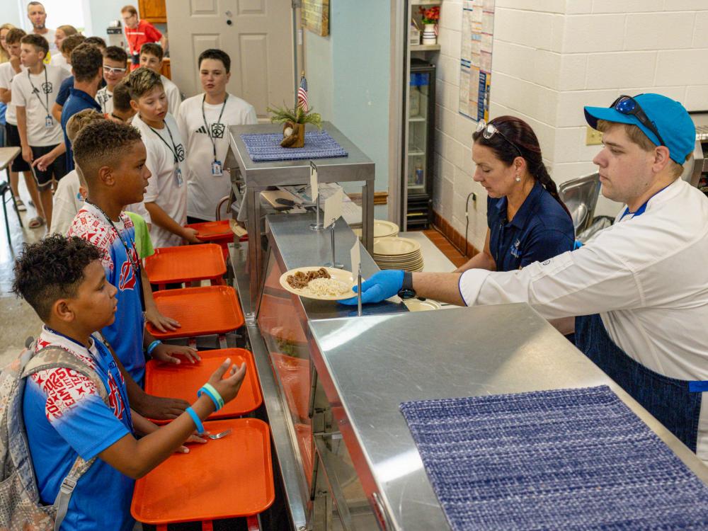 Two staff members serve lunch to little league baseball players